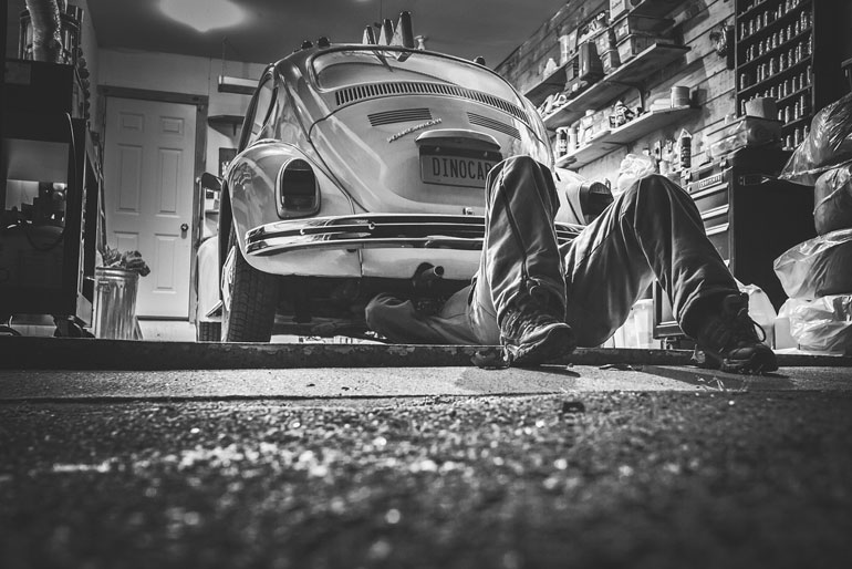 A car mechanic under a car that is located in a car shop.